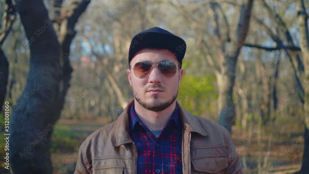 A tough guy in a leather jacket, a black baseball cap and stylish glasses and looks spectacularly at the camera with a serious expression on his face. Waiting for someone. Be free and wild. A tough guy in a leather jacket, a black baseball cap and stylish glasses and looks spectacularly at the camera with a serious expression on his face. Waiting for someone. Be free and wild.