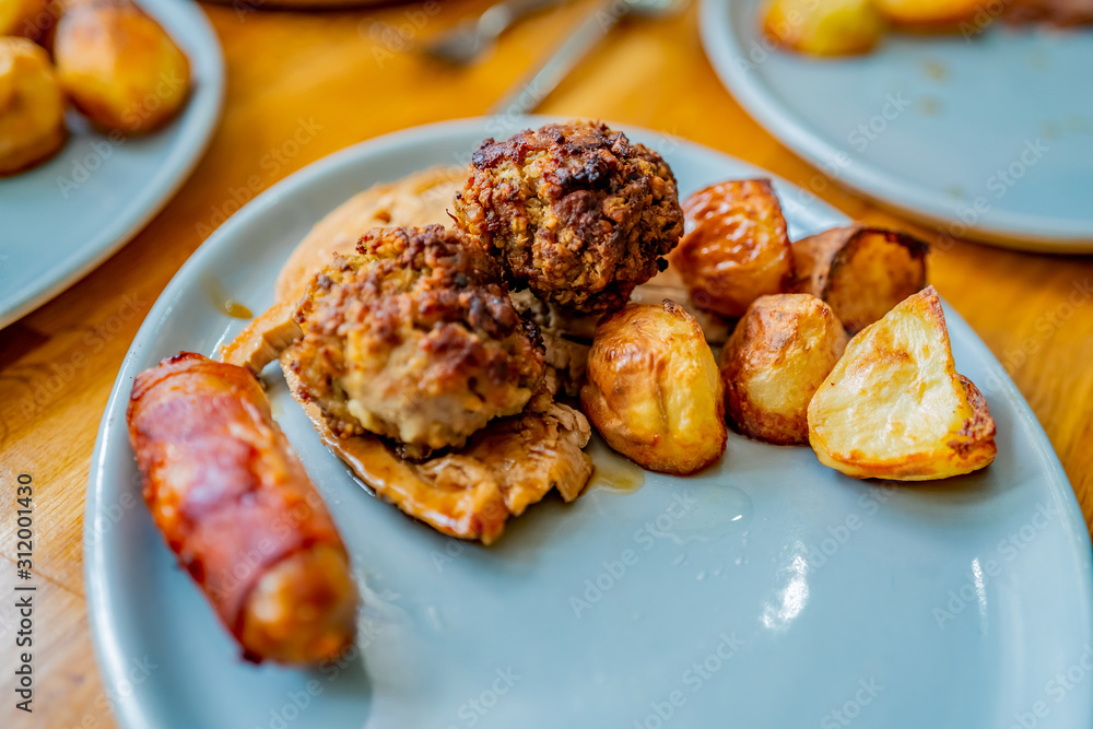 Selective focus of roast potatoes together with slice of roast turkey, stuffing ball and pig in blanket on a blue oval dinner plate Selective focus of roast potatoes together with slice of roast turkey, stuffing ball and pig in blanket on a blue oval dinner plate