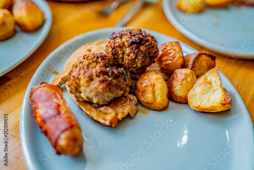  Selective focus of roast potatoes together with slice of roast turkey, stuffing ball and pig in blanket on a blue oval dinner plate
