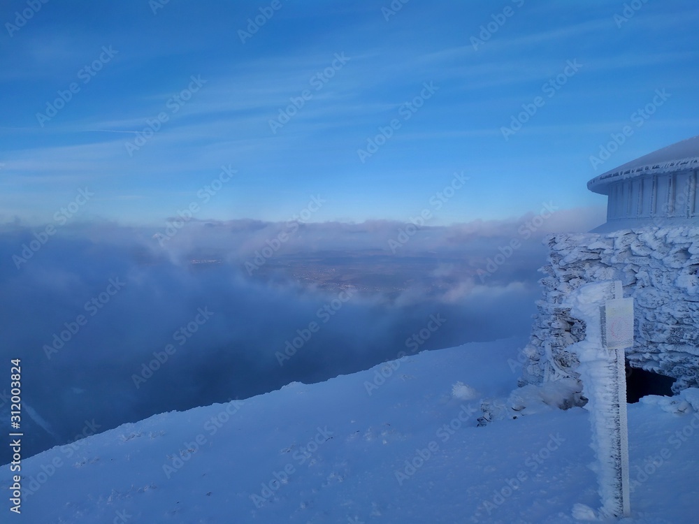 Beautiful winter sunny day in Krkonose Mountains. The highest peak Snezka with its frozen weather station. Clouds in the valley. Beautiful winter sunny day in Krkonose Mountains. The highest peak Snezka with its frozen weather station. Clouds in the valley.