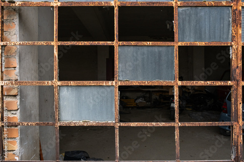 The broken windows and rusting frame of a door leading into a garage, nobody in the image