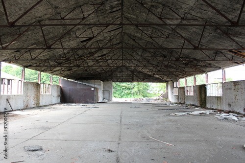 Fototapeta Naklejka Na Ścianę i Meble -  Inside of large empty military hangar with destroyed inner walls and missing windows at abandoned military complex on warm sunny summer day