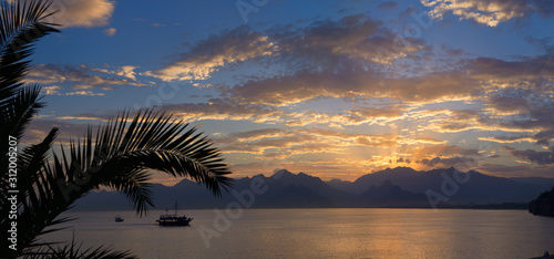 Panorama of Antalya Harbour Turkey with sunset sunbeams over mountains palm tree and tall ship