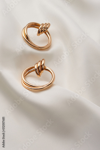 Subject shot of a pair of golden earrings isolated on the white textile surface. Each earring is made as a set of three glossy rings and a large double hoop