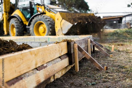 Excavation works at the construction site. Bulldozer or a backhoe loader dumping ground into the falsework. Low-rise construction. Foundation of  small cottage