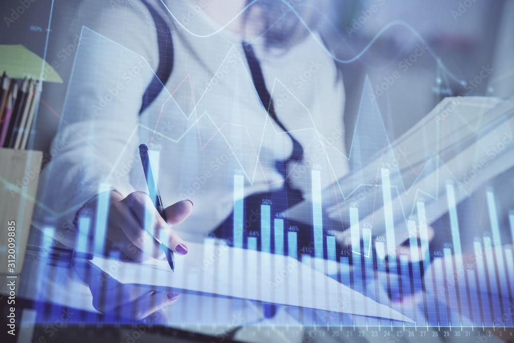 A woman hands writing information about stock market in notepad. Forex chart holograms in front. Concept of research. A woman hands writing information about stock market in notepad. Forex chart holograms in front. Concept of research.