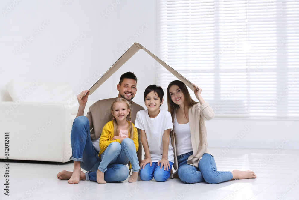 Happy family sitting under cardboard roof at home. Insurance concept Happy family sitting under cardboard roof at home. Insurance concept