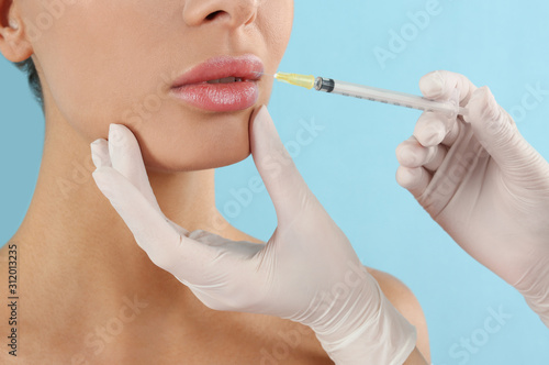 Woman getting lip injection on light blue background  closeup