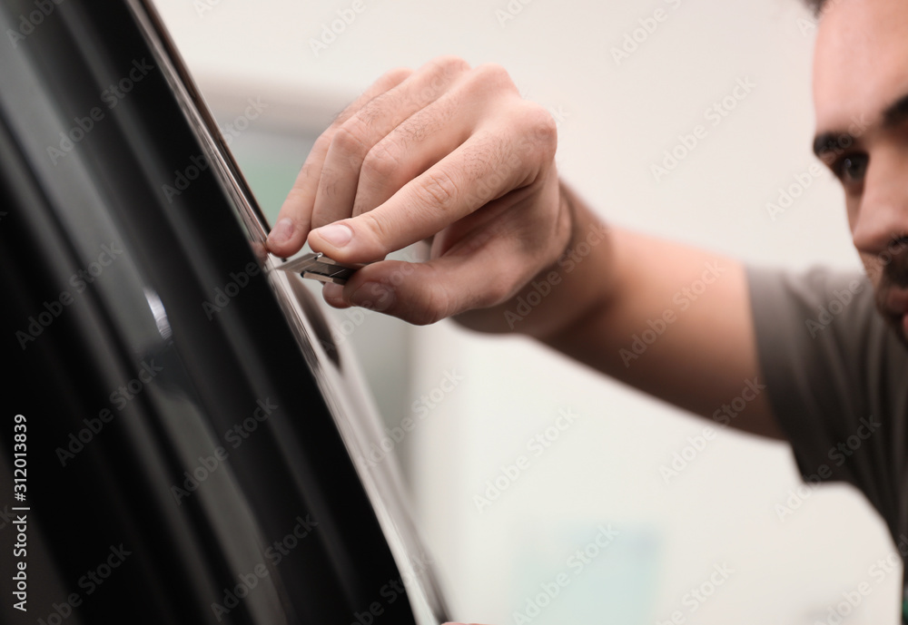 Worker tinting car window with foil in workshop, closeup Worker tinting car window with foil in workshop, closeup