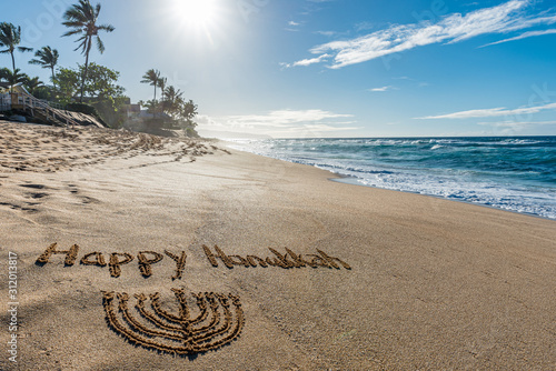 Happy Hanukkah written in the sand with a Hanukkiah with a tropical beach and ocean in the background