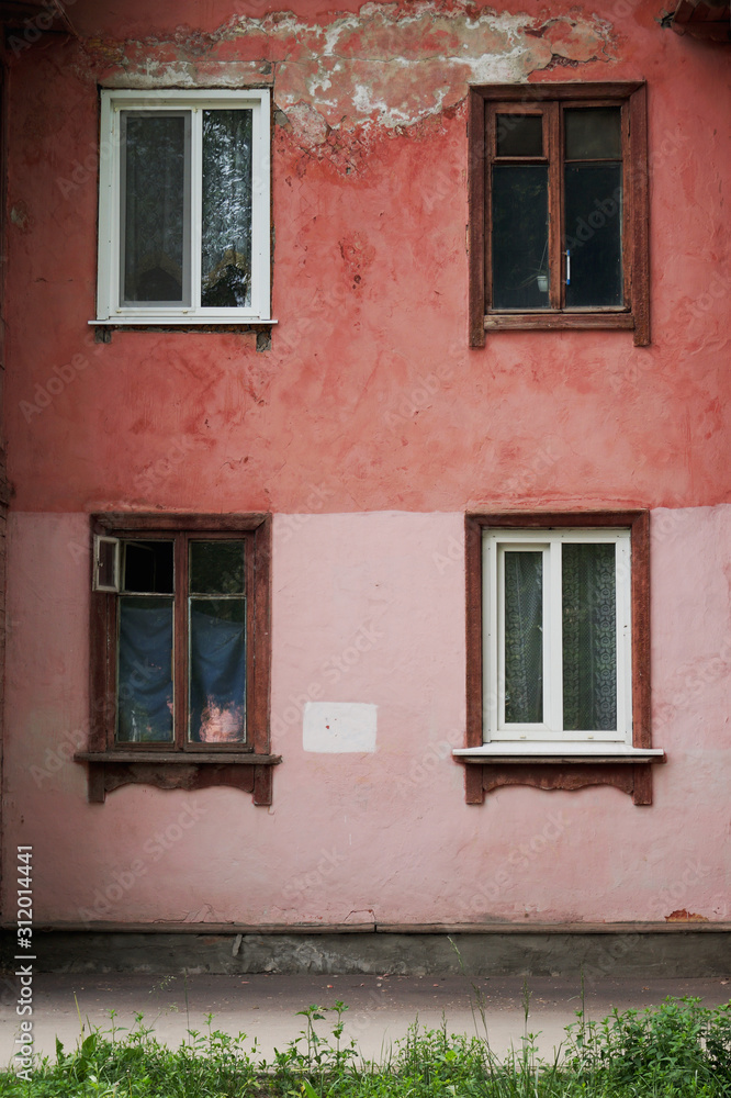 The facade of an old building with four contrasting Windows: frames made of wood and plastic. Falling off plaster pink. Vertical position.