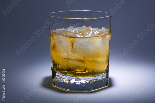 A glass of whiskey with ice. Art installation with lighting from above and close-up.