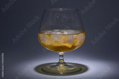 A glass of whiskey with ice. Art installation with lighting from above and close-up.