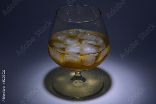 A glass of whiskey with ice. Art installation with lighting from above and close-up.