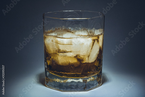 A glass of whiskey with ice. Art installation with lighting from above and close-up.