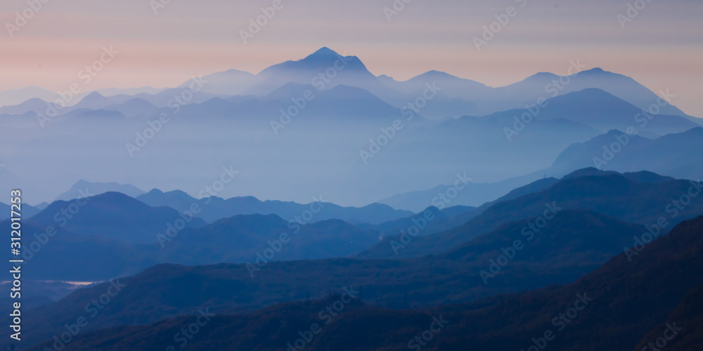  with blue misty mysterious mountains in the distance and an orange pastel sky. Distant blue mountains.