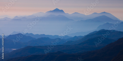  with blue misty mysterious mountains in the distance and an orange pastel sky. Distant blue mountains. © Mikhail Semenov