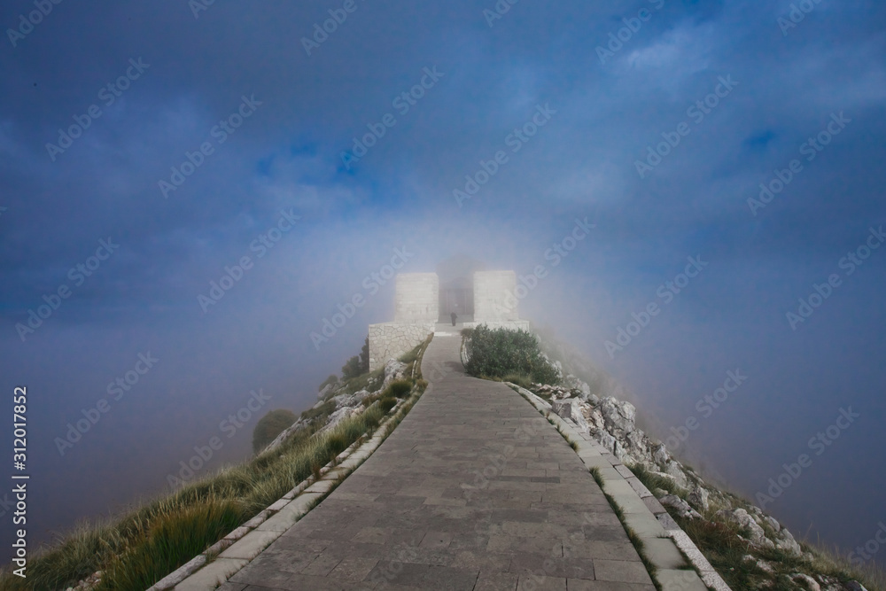 foggy  road in the clouds stone path,  road lined with slabs goes along a high pass to the observation deck, blue sky stones and grass summer-autumn Montenegro, mountain Lovcen.