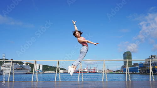 beautiful sporty girl in life style clothes jumping dance pose on the observation deck on a sunny day. circus gymnast in the port in denim casual wear. acrobatic jumping 