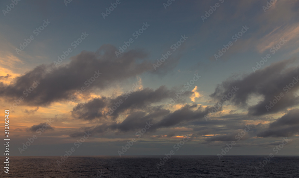 A dramatic set of clouds, at sunset, drifting over the tropical waters of the Caribbean Sea are lit by the last moments of daylight.