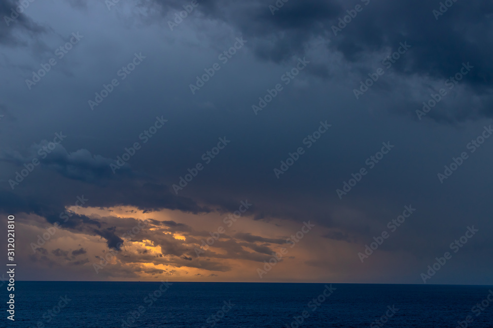 A dramatic set of clouds, at sunset, drifting over the tropical waters of the Caribbean Sea are lit by the last moments of daylight.