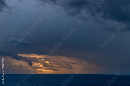 A dramatic set of clouds, at sunset, drifting over the tropical waters of the Caribbean Sea are lit by the last moments of daylight.