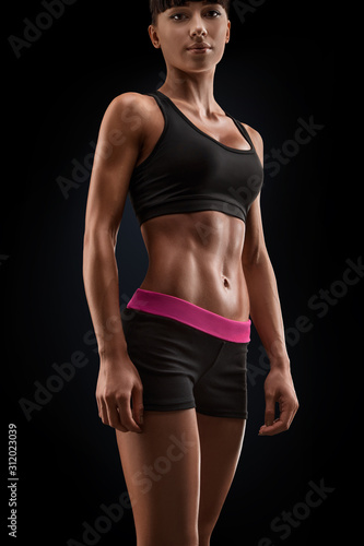 Beautiful sexy female slim tanned body. Cheerful attractive young fitness woman in black top and black shorts isolated over black background © USM Photography
