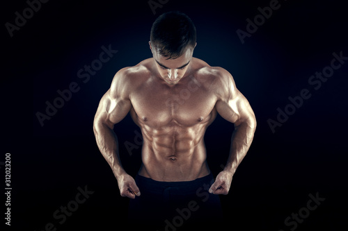 Strong athletic man fitness model torso showing six pack abs, perfect abs, shoulders, biceps, triceps and chest. Isolated on black background.