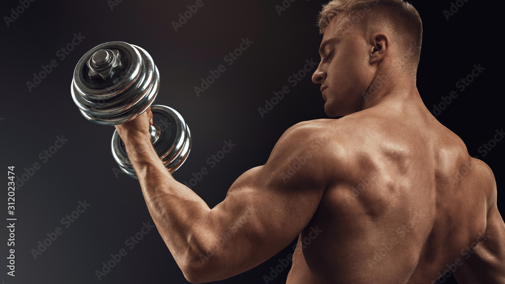 Closeup of a handsome power athletic man bodybuilder doing exercises with dumbbell. Fitness muscular body on dark background. Closeup of a handsome power athletic man bodybuilder doing exercises with dumbbell. Fitness muscular body on dark background.