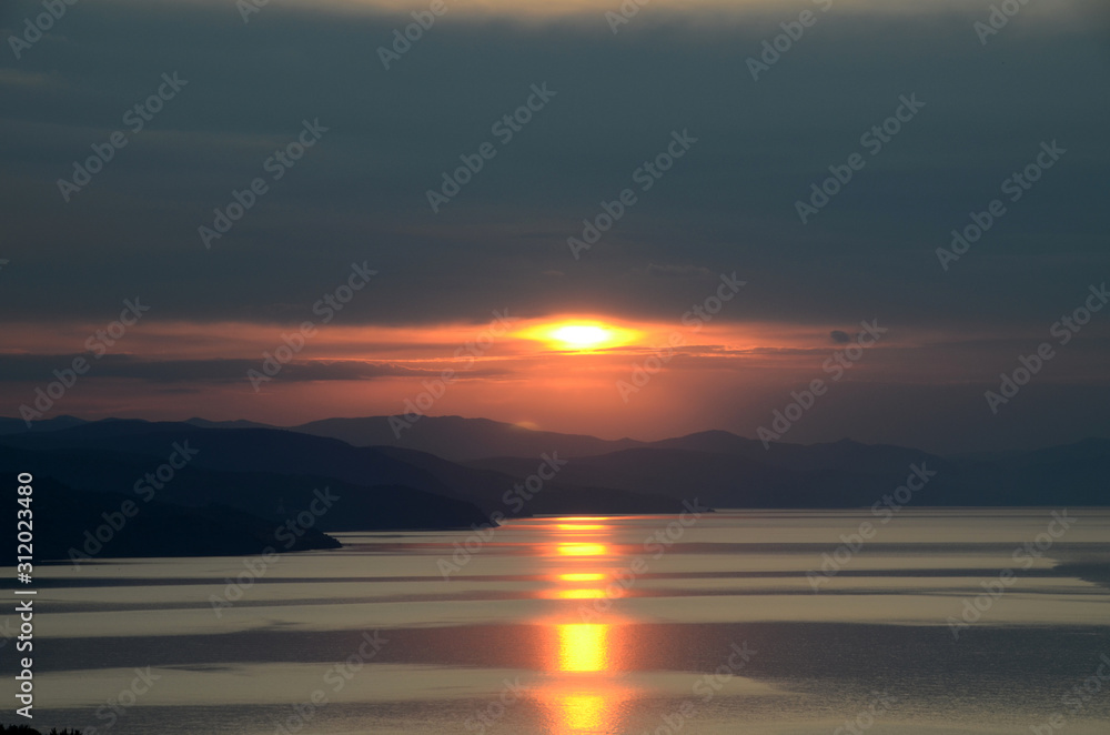 Glare dawn over the distant hills with a vivid yellow track on the sea. Sunrise over the vast aquatics area of Black Sea, Crimea
