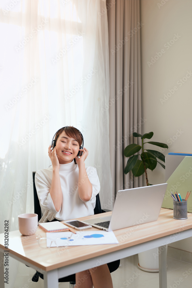 Young Asian woman in headphones working on the computer at home Young Asian woman in headphones working on the computer at home