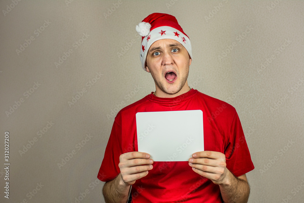 young guy in christmas hat and red t-shirt with white card in his hands for inscription young guy in christmas hat and red t-shirt with white card in his hands for inscription