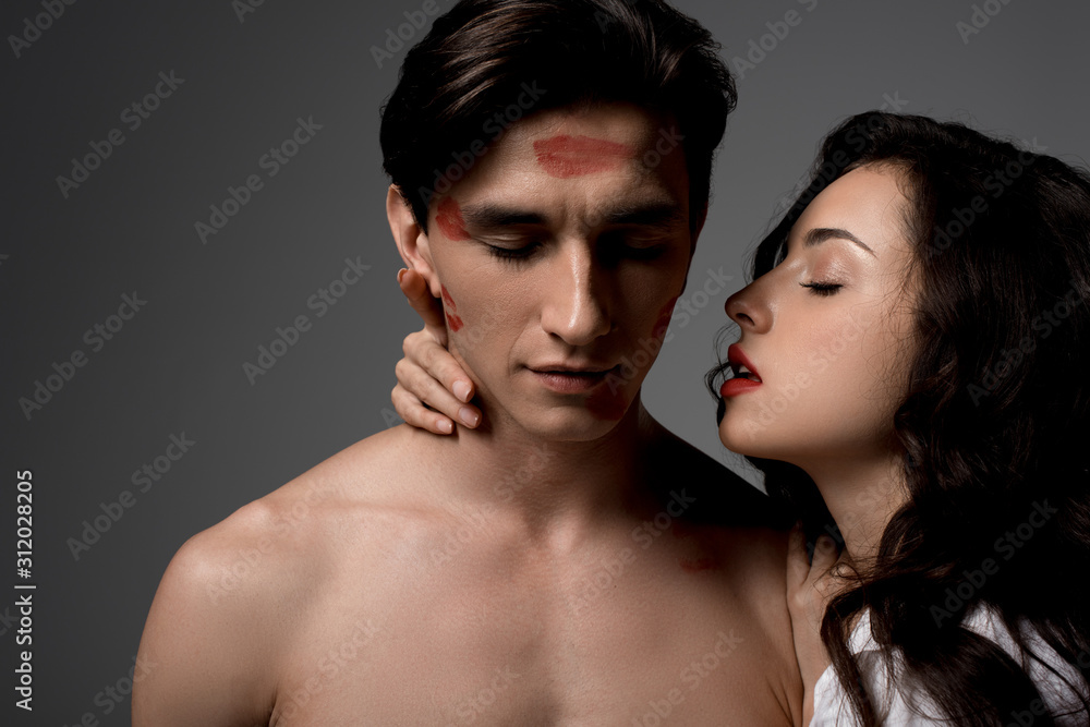 attractive passionate girl hugging man with red lipstick prints, isolated on grey attractive passionate girl hugging man with red lipstick prints, isolated on grey