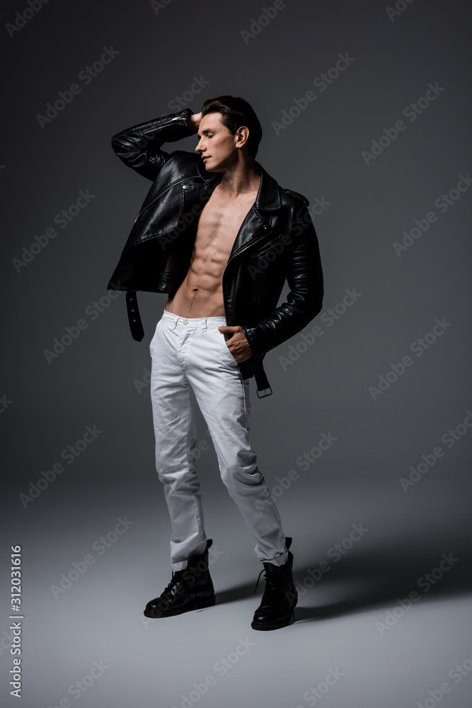 young sexy man in white jeans and black leather jacket, on grey young sexy man in white jeans and black leather jacket, on grey