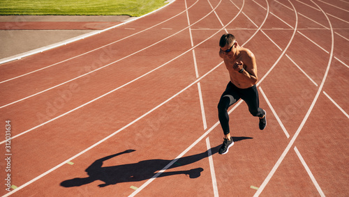 Horizontal image of young man athlete running on a track race in stadium. Athletic male jogging on a sunny day at stadium. People, healthy lifestyle and sport concept © iuricazac