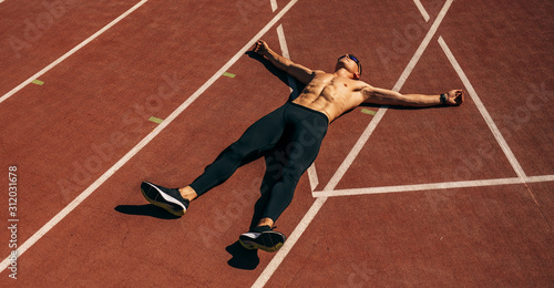 Overhead view image of young handsome shirtless athlete man lying on racetrack at stadium taking rest. Professional sportsman resting after training session. People, sport and healthy lifestyle © iuricazac