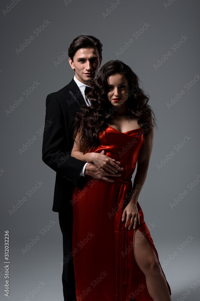 passionate couple in suit and red silk dress hugging on grey passionate couple in suit and red silk dress hugging on grey