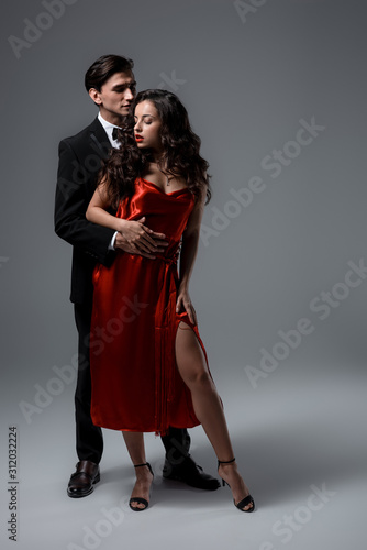 sensual couple in suit and red silk dress hugging on grey