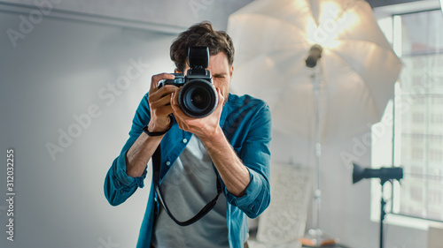 In the Photo Studio with Professional Equipment: Portrait of the Famous Photographer Holding State of the Art Camera Taking Pictures with Softboxes Flashing in Background. photo