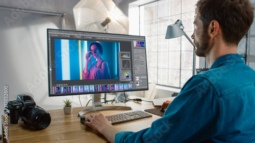 Professional Photographer Sitting at His Desk Uses Desktop Computer in a Photo Studio Retouches. After Photoshoot He Retouches Photographs of Beautiful Female Model in an Image Editing Software photo