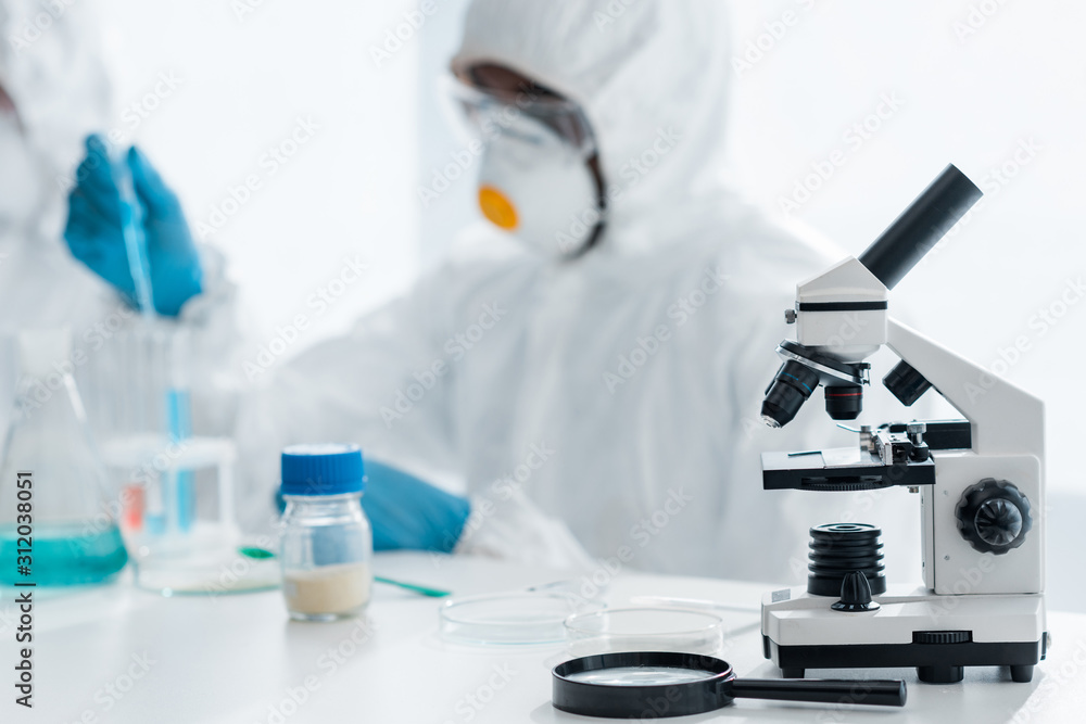 selective focus of microscope and magnifying glass on table and african american scientist working in lab selective focus of microscope and magnifying glass on table and african american scientist working in lab