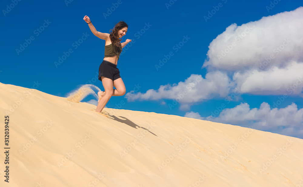 ein Mädchen rennt im Sommer voller Lebensfreude von einer Sanddüne und wirbelt dabei Staub auf ein Mädchen rennt im Sommer voller Lebensfreude von einer Sanddüne und wirbelt dabei Staub auf