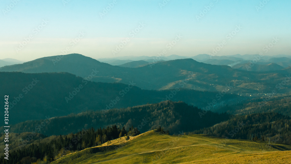 Fototapeta premium Beautiful sunny landscape with mountains and trees. Blue sky, grass and forest. Background or wallpaper.
