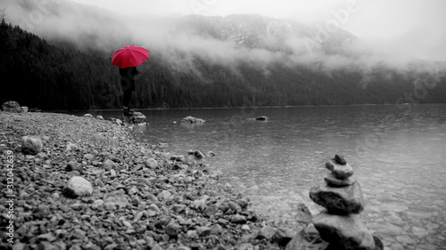 Walk around the Eibsea (Eibsee) near Zugspitze (highest mountain in Germany). Rainy weather. Sea surrounded with fir trees, stones and rock fragments. Wanderer with red umbrella. Black and white.