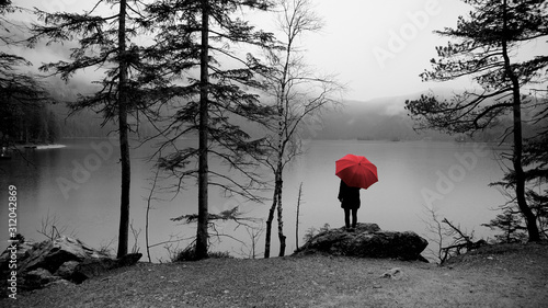 Wanderung um den Eibsee am Fuß der Zugspitze. Wanderer mit rotem Regenschirm. Bild in schwarz weiß.