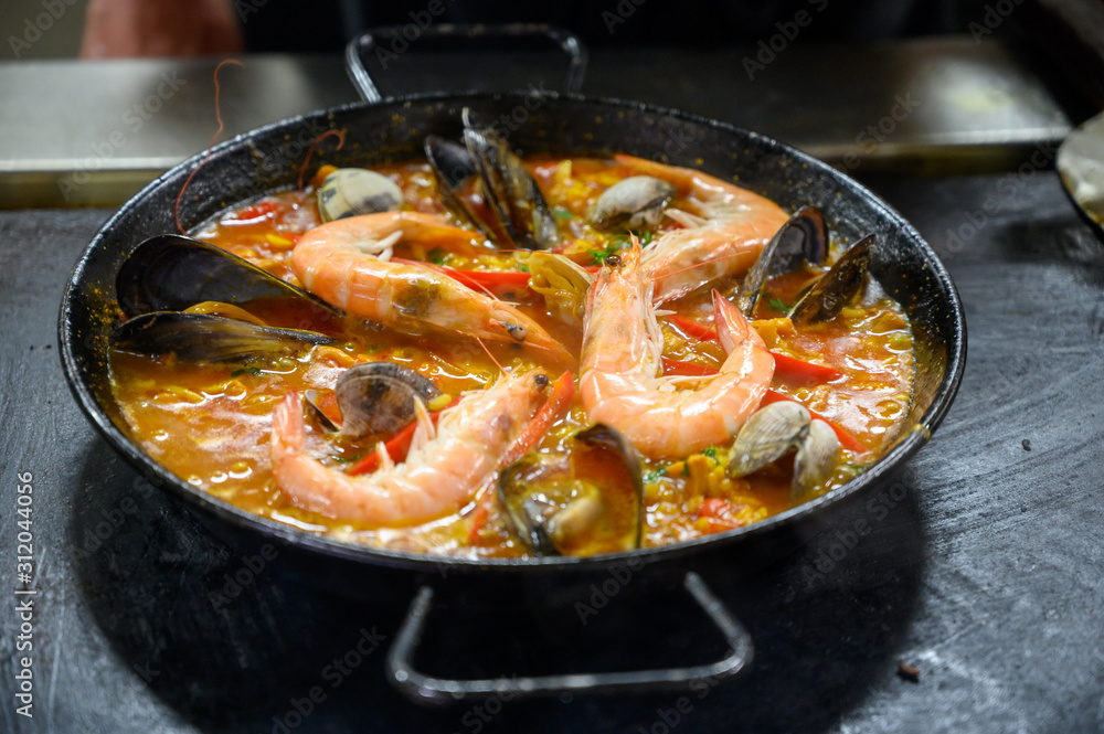 Spanish cuisine, man making paella, famous dish with rice and seafood from Valencia Spanish cuisine, man making paella, famous dish with rice and seafood from Valencia