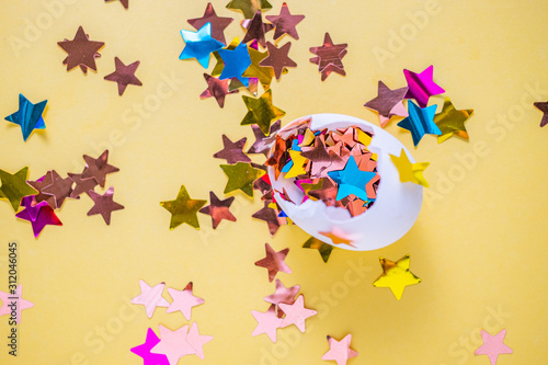 Egg with star shaped colourful confetti on yellow background. Festive decorations