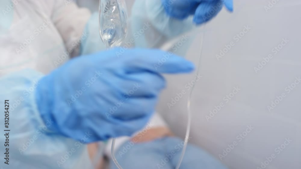 Sequence of shots of nurse preparing fluid bag and giving IV therapy to young female patient lying on medical couch in hospital ward Sequence of shots of nurse preparing fluid bag and giving IV therapy to young female patient lying on medical couch in hospital ward