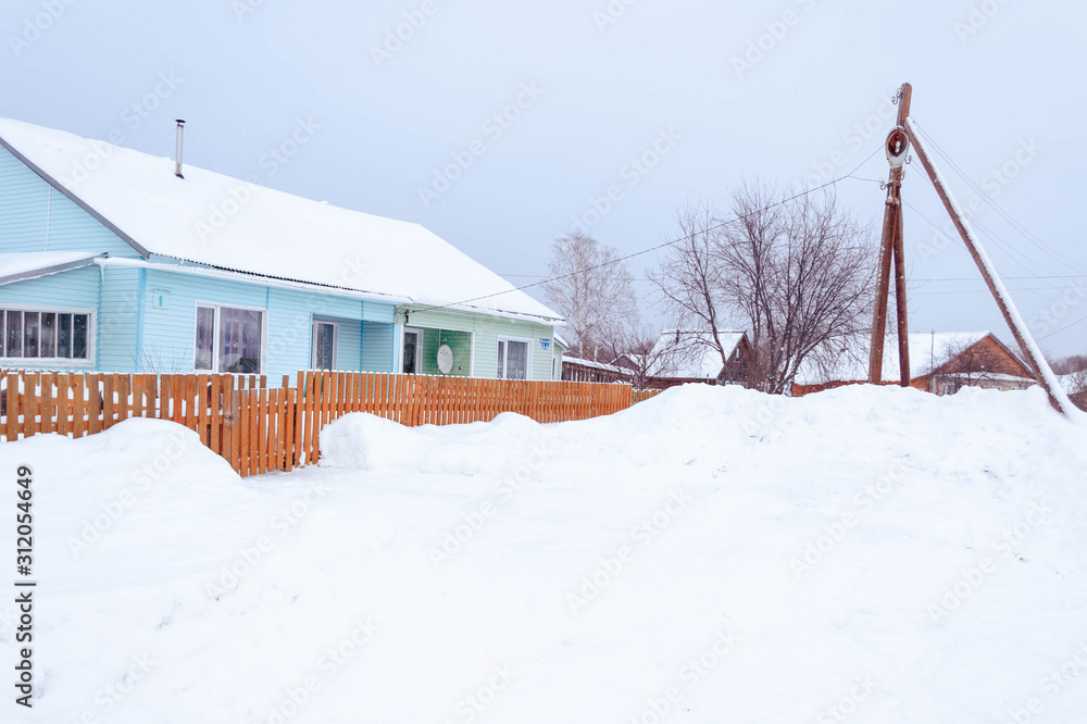 village in winter in the snow on a sunny day. street of wooden houses road at houses near the forest, no people. village in winter in the snow on a sunny day. street of wooden houses road at houses near the forest, no people.