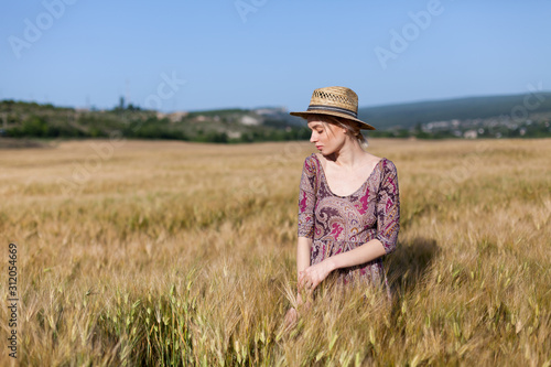 portrait of a beautiful fashionable blonde woman in a hat in a field of ripe wheat